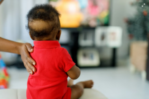 This image shows a baby being supported in a sitting position, representing early childhood care and developmental observation