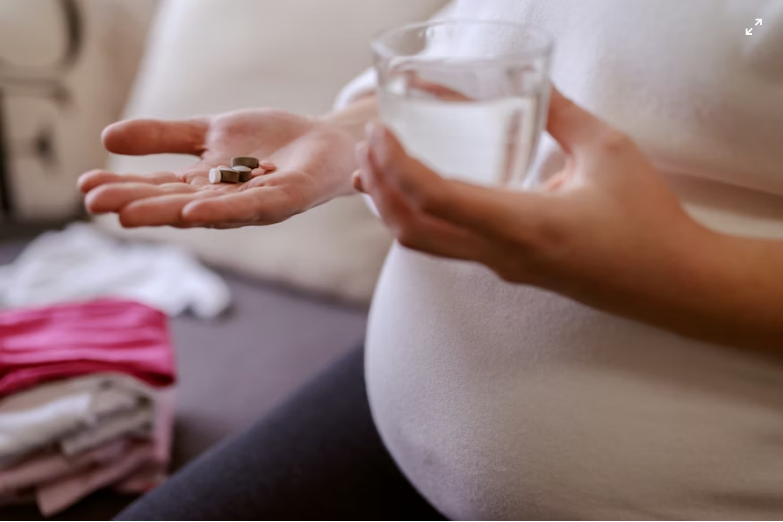 This is an image of a pregnant woman holding some pills and a glass of water.