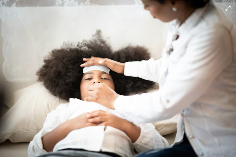 This is an image of a mother giving a sick child medicine while checking their temperature at home