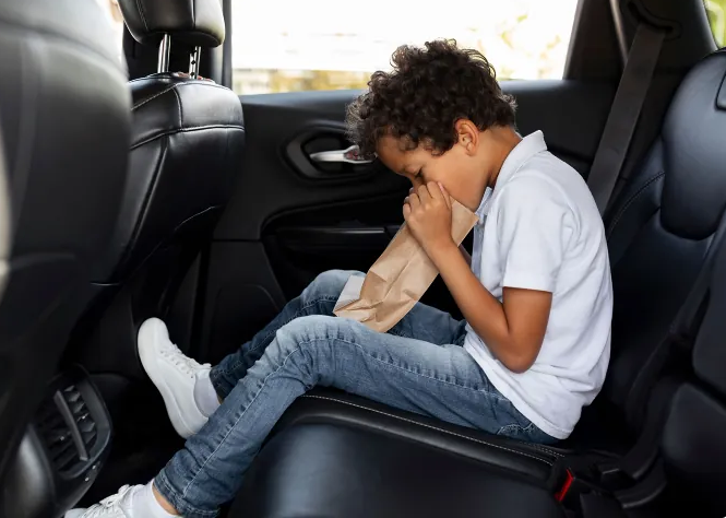An image of a little boy throwing up in a paper bag, in a car