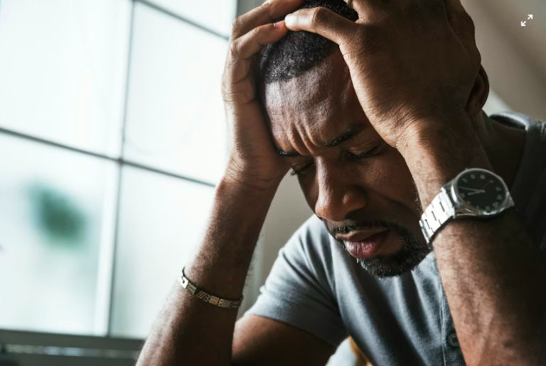 An image of a man holding his head with both hands, showing discomfort from a headache.