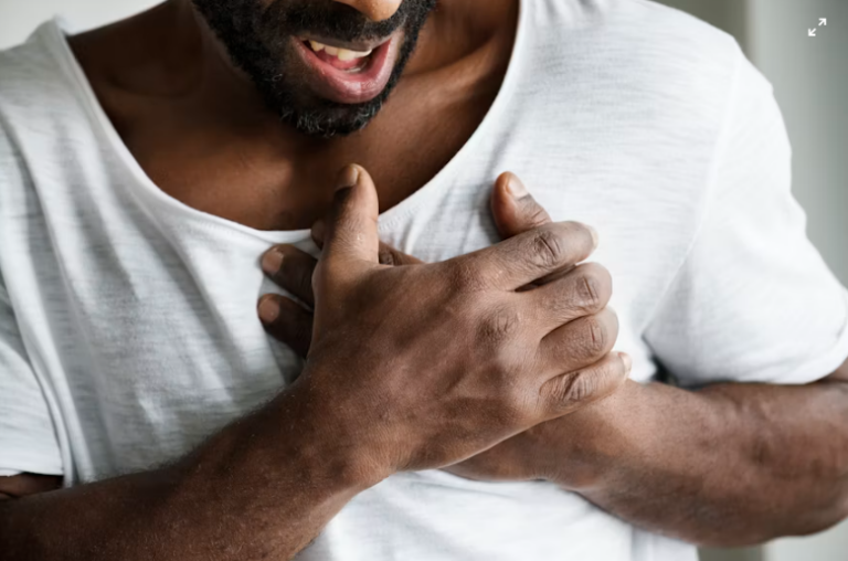 An image of a man holding his chest with both hands showing chest pain or discomfort.