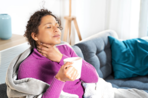 An image of a woman sitting down and holding her throat due to an itchy or irritated throat.