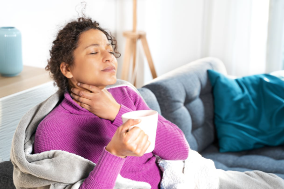 An image of a woman sitting down and holding her throat due to an itchy or irritated throat.