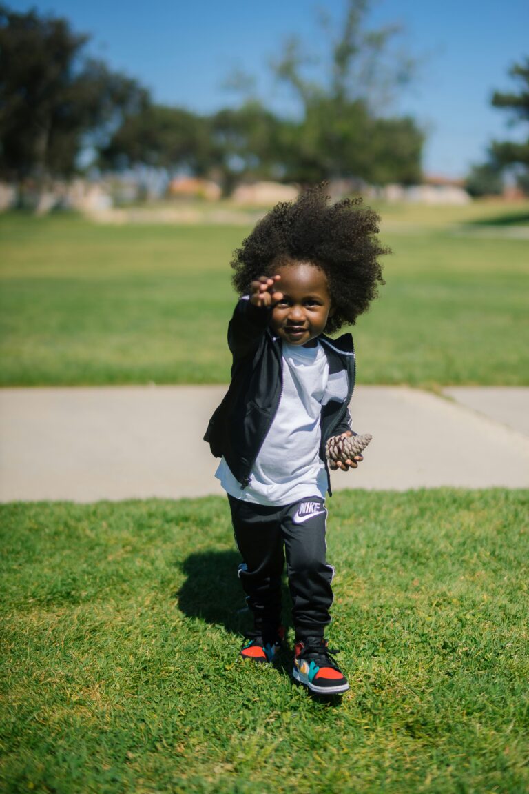 A happy toddler walking across a grassy yard outdoors, smiling while exploring the surroundings.