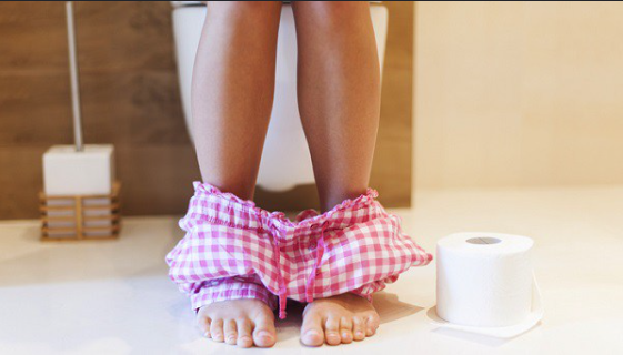 An image of a woman sitting on a toilet in a bathroom, shown from the knees down